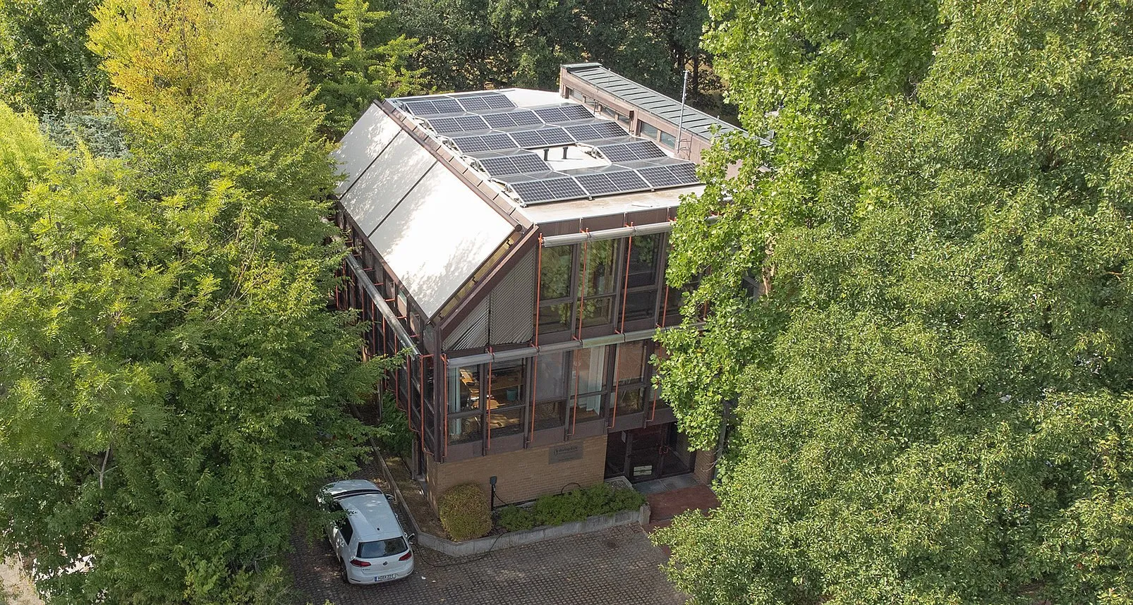 Luftbild des Firmensitzes von dialog EDV in Hannover mit Photovoltaikanlage auf dem Dach, umgeben von Bäumen