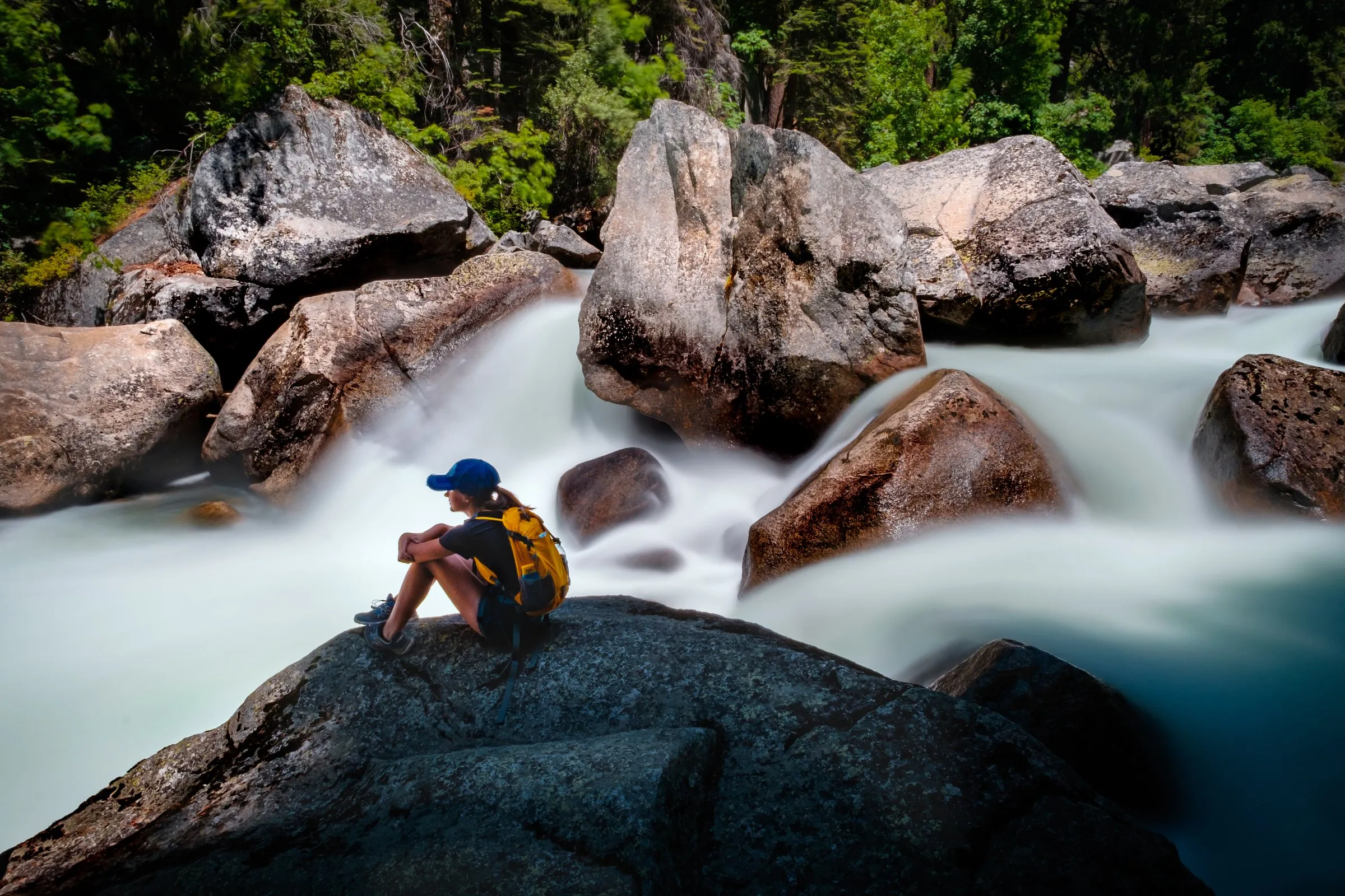 Person sitzt ruhig auf einem Felsen vor tosendem Wildwasser