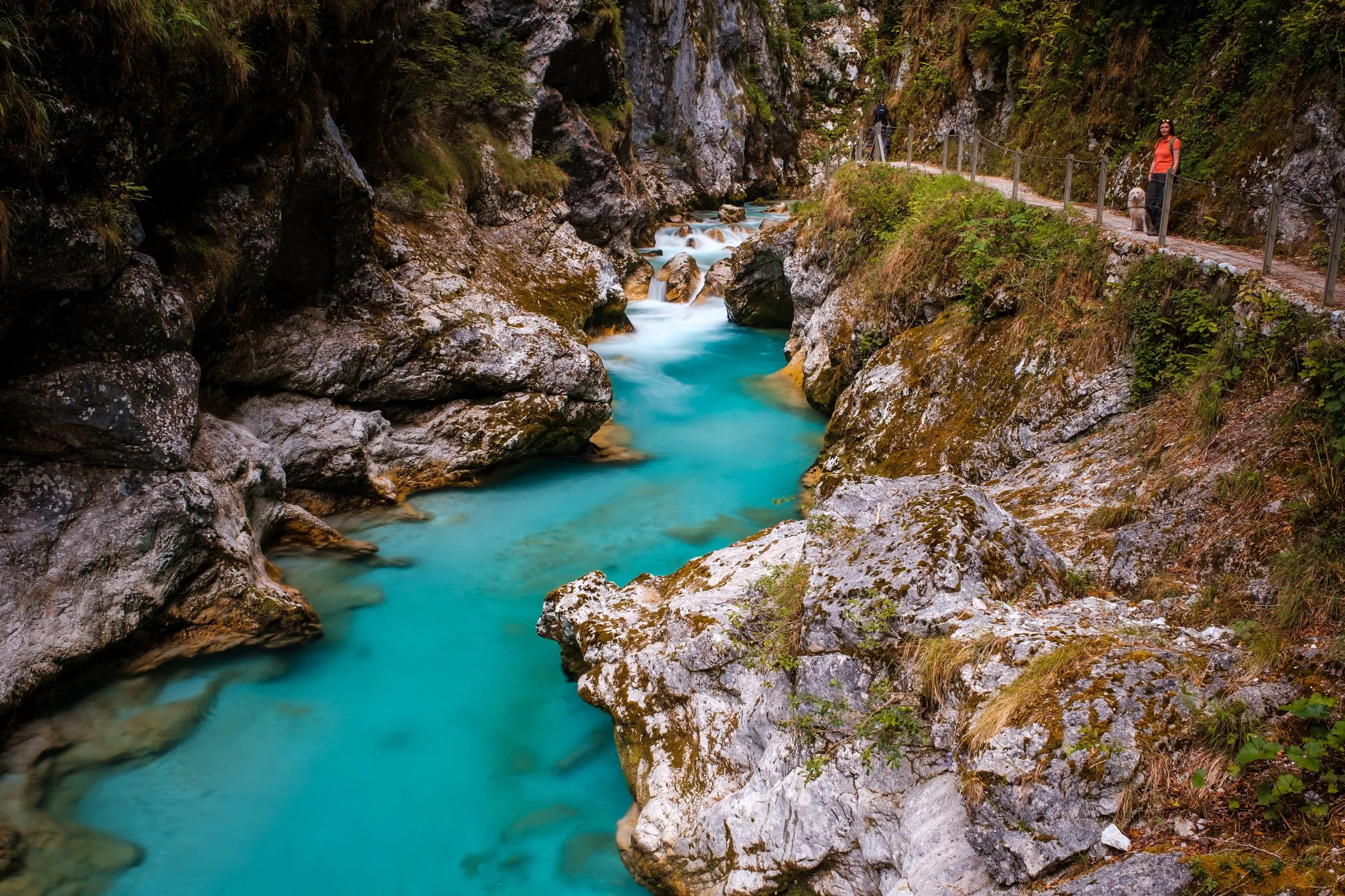 Wanderer auf einem gesicherten Weg über einer Schlucht mit türkisfarbenem Fluss