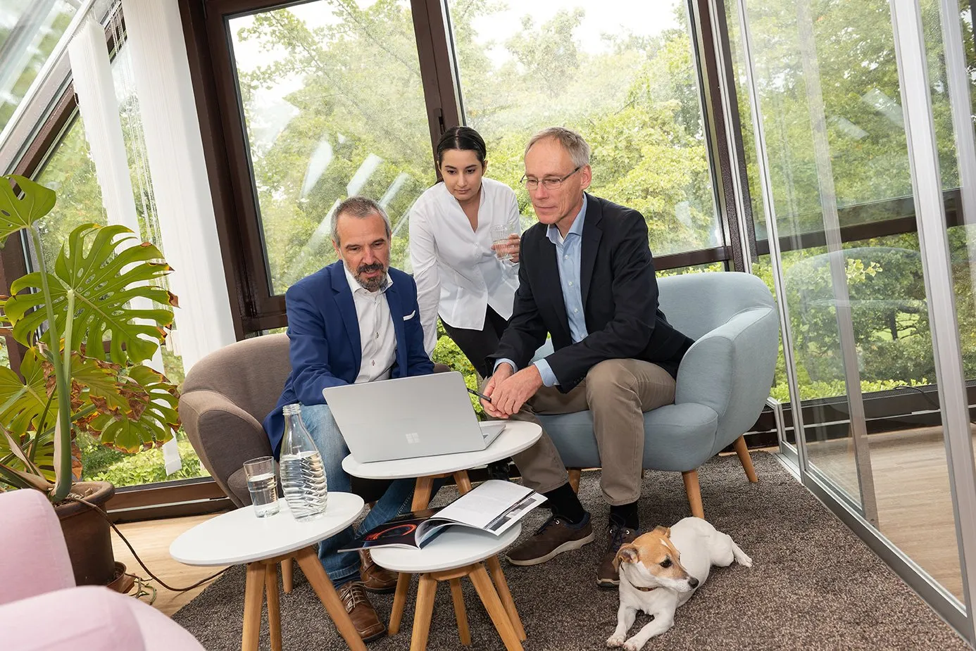Drei Mitarbeitende von dialog EDV besprechen sich am Laptop im Wintergarten, daneben liegt ein Hund